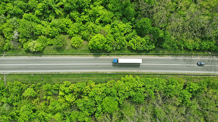 An aerial view of a truck on a highway with trees on both sides